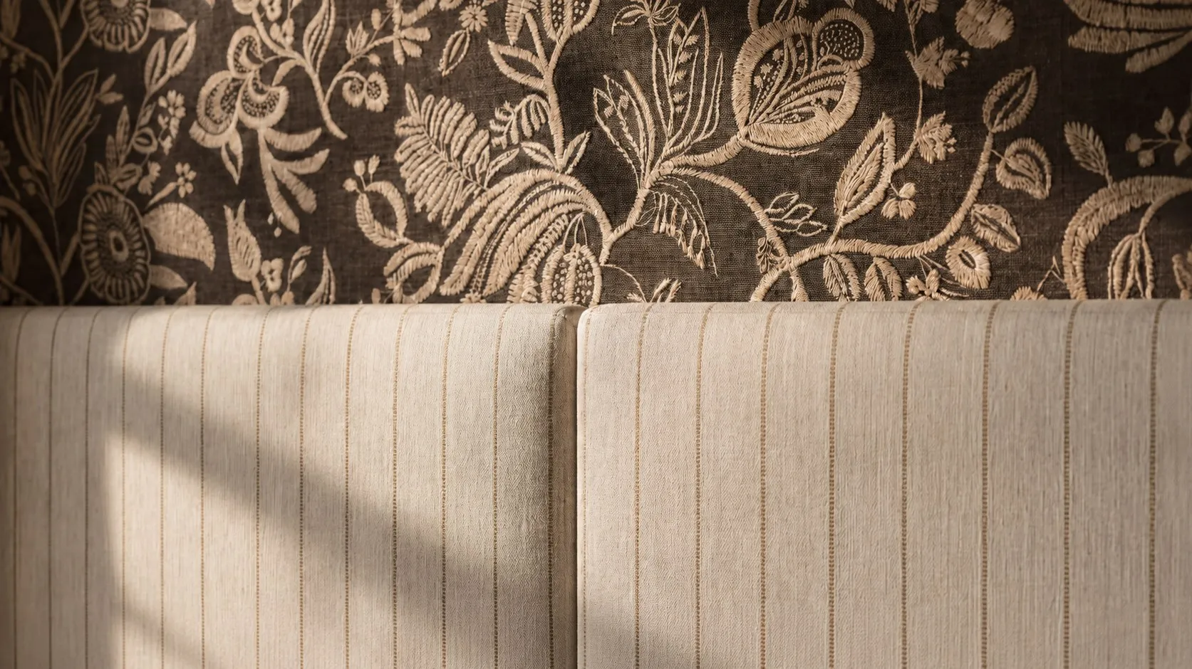 Detail of the upholstered, panelled headboard wall meeting the botanical wallpaper